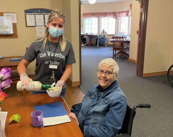 Senior living worker helps a senior woman with her meal at a senior living facility in Colby, Wisconsin.