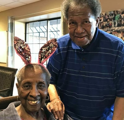 Senior man and woman with bunny ears smile at the camera at a senior living community in Omaha, Nebraska.