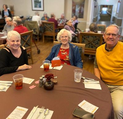 Two senior women and a senior man enjoy drinks together in the dining room