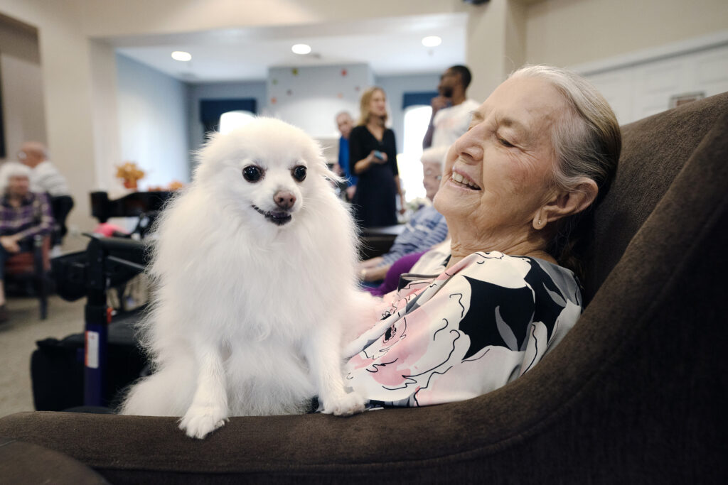 Senior woman smiles with a small white dog on her lap