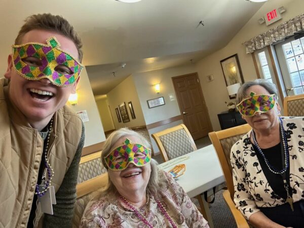 an employee and two senior women smile with Mardi Gras masks on