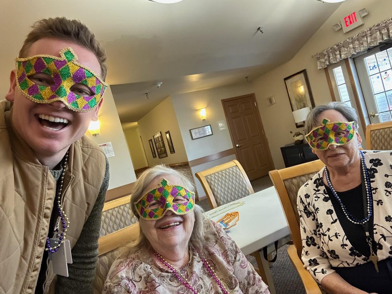 an employee and two senior women smile with Mardi Gras masks on