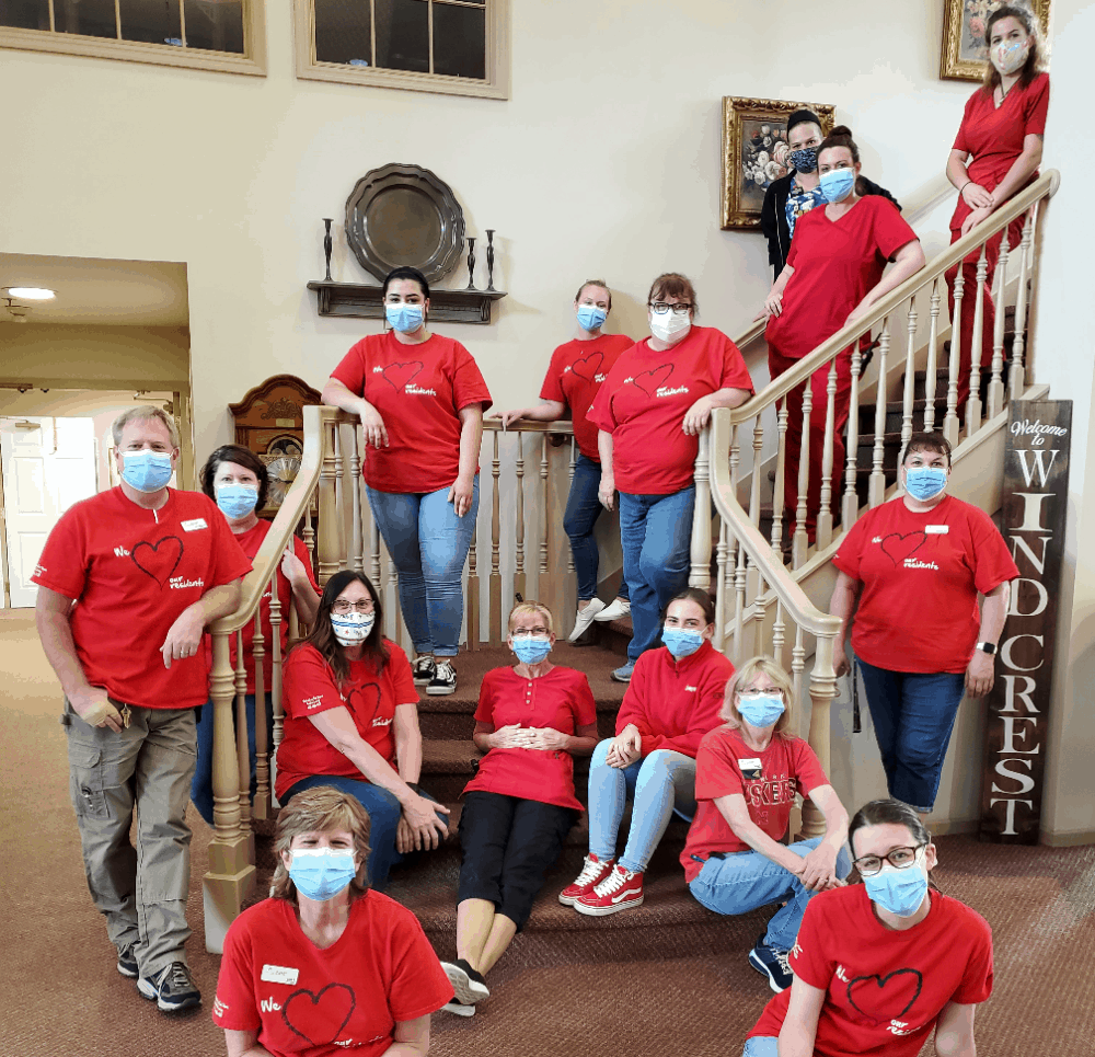 Employees-pose-in-face-masks-and-red-shirts-on-staircase-in-senior-living-facility.