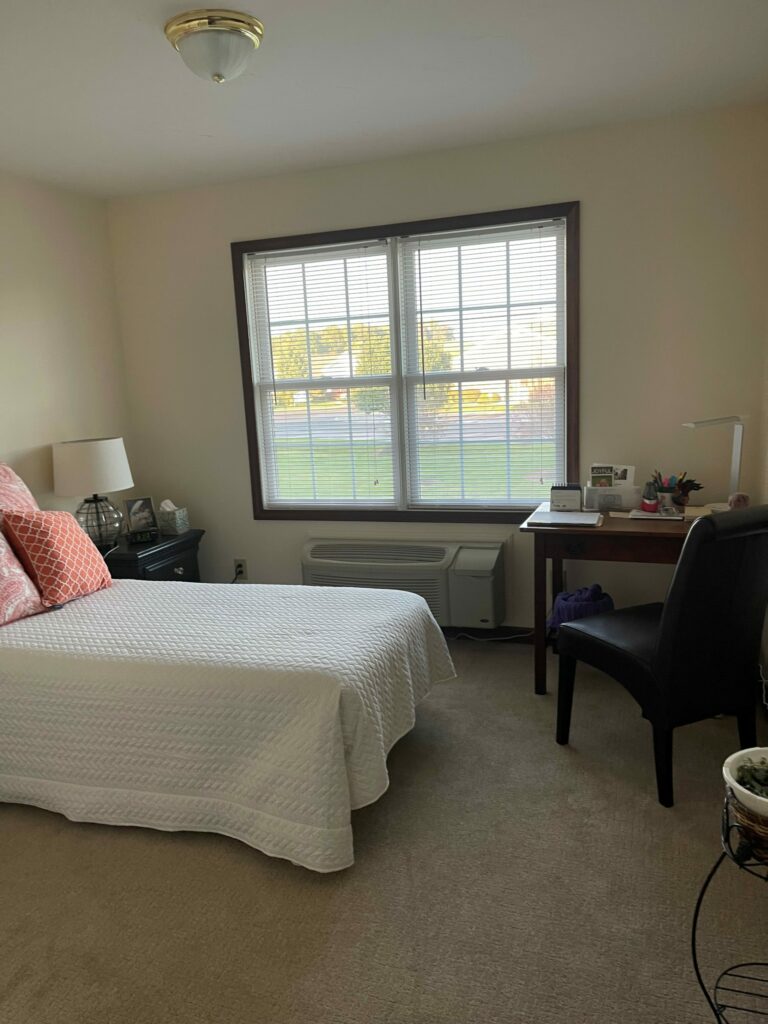 small bed and desk near a window within a senior apartment