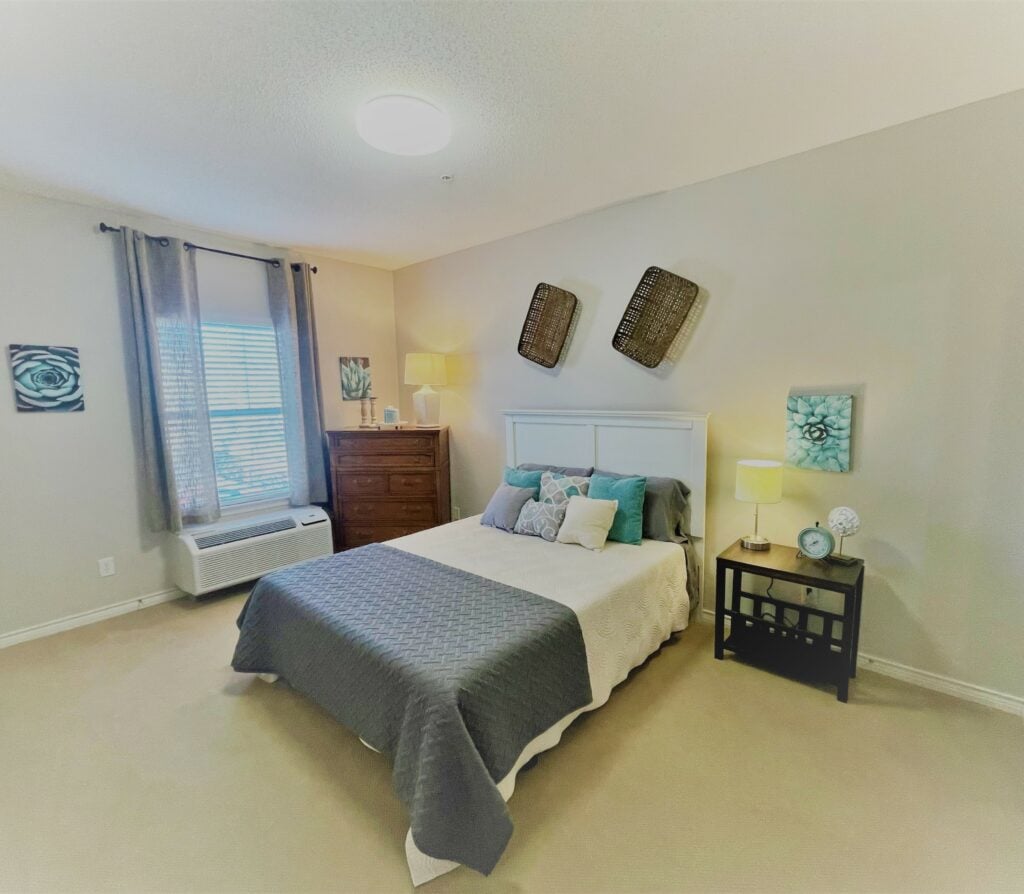 apartment bedroom with a dresser near a window, a large bed and side table