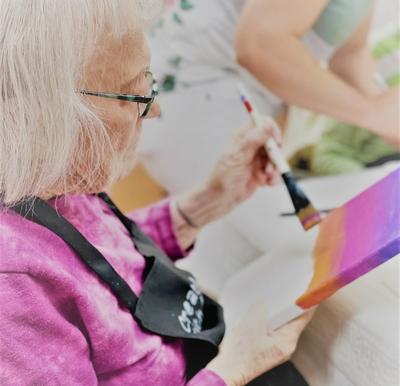 senior woman paints a sunset on a canvas