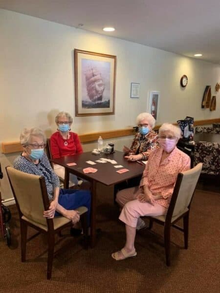 Four senior women with masks on play cards at a senior living community in Irving, Texas.