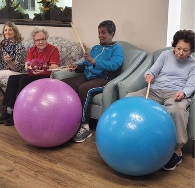 four senior women work out together by playing the drums on exercise balls
