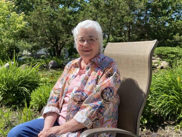 senior woman smiles while seated in a chair outside