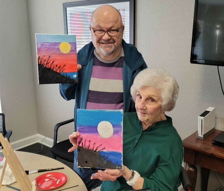 senior man and senior woman pose with their completed canvas paintings