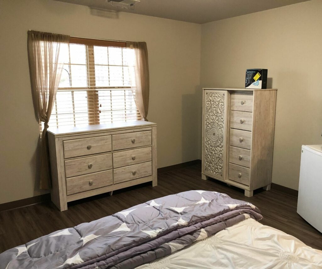 senior apartment with a dresser by a window and other shelving near a bed