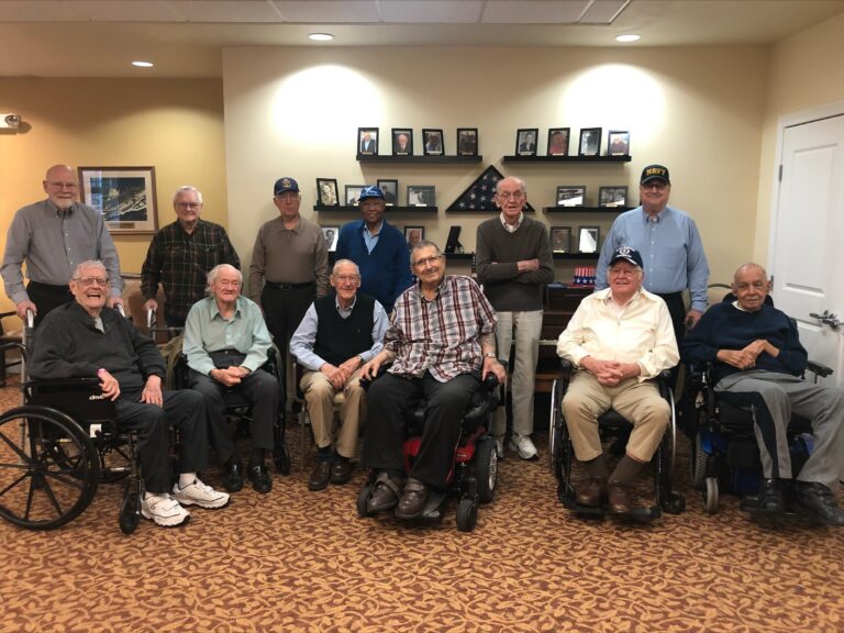 group of senior men smile and pose near the Wall of Honor