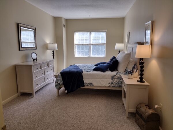 apartment bedroom with a large bed, dresser, side tables and window