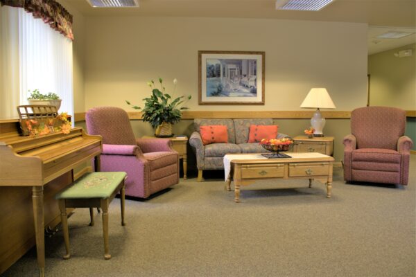 a couch and two chairs sit near a piano in a senior living community in West Bend, WI.