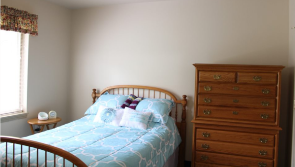 Model apartment bedroom with bed, dresser and window at a senior living community in West Bend, Wisconsin.