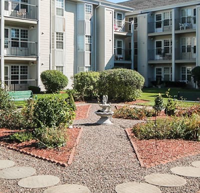 A well-landscaped courtyard with a paved walking path and fountain feature in Williamsville, New York.