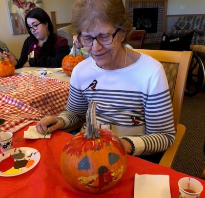 A smiling resident painting a pumpkin during a fall activity session in Plymouth, Wisconsin.