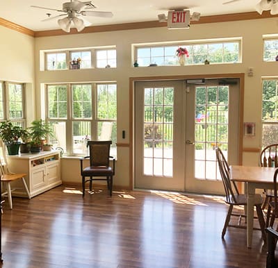 A bright sunroom with large windows and doors, seating and a piano in Plymouth, Wisconsin.