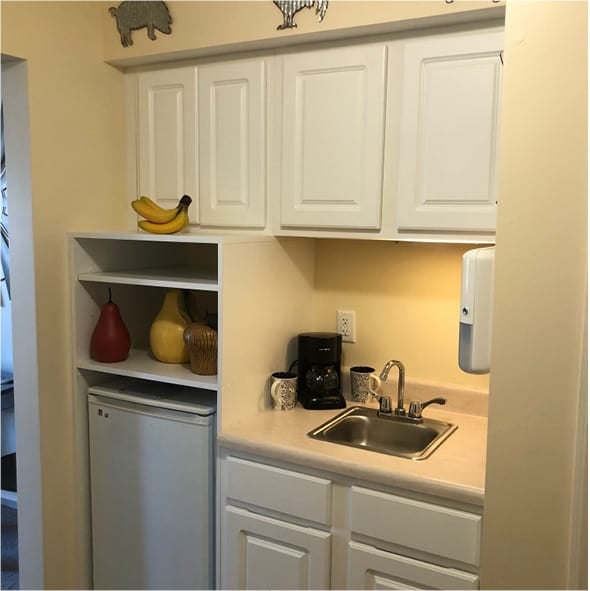 A kitchenette with white cabinetry, a sink and small refrigerator in Hamilton, Ohio.