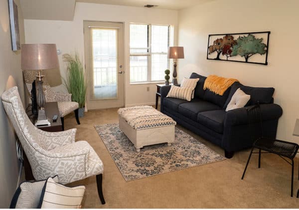 A bright, beautiful living room in a model apartment with plenty of comfortable seating and a door leading out to a patio in Williamsville, New York.