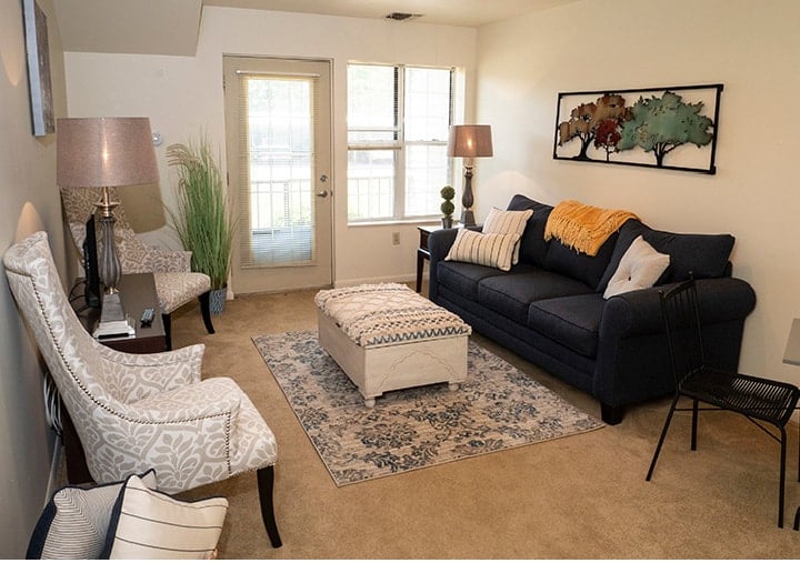 A bright, beautiful living room in a model apartment with plenty of comfortable seating and a door leading out to a patio.