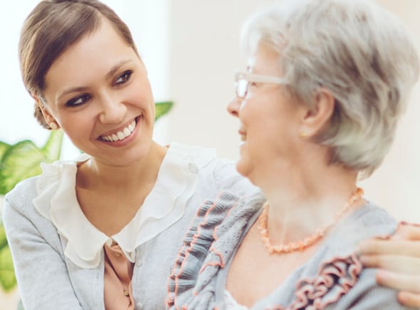 A smiling caregiver with her arm around a memory care resident.