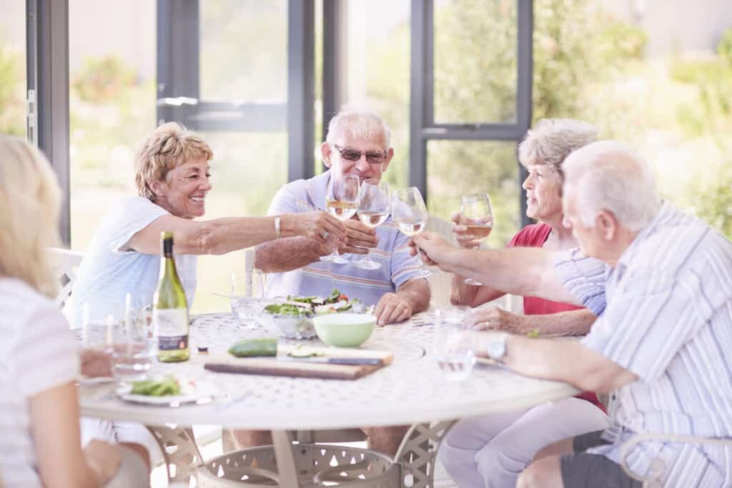 Senior adults toasting wine glasses at patio lunch.