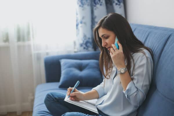 Girl talking on the phone on a blue sofa in a real interior against the window.