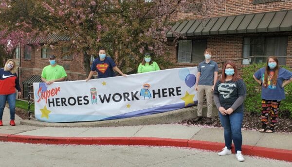 A group of employees wearing masks, social distancing and holding up a sign that says "HEROES WORK HERE".