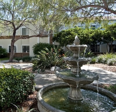 A beautiful, serene fountain in a well-maintained, landscaped courtyard with rich foliage and tree covering providing ample shade along the walking paths in Corpus Christi, Texas.