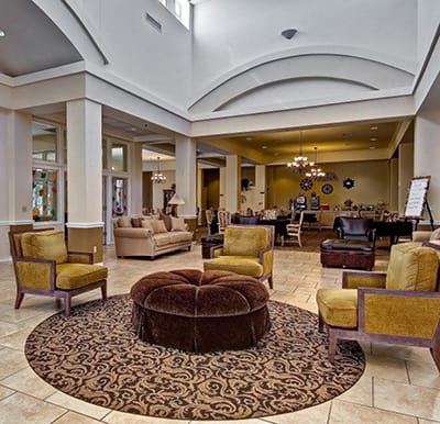 A beautiful lounge area with richly upholstered seating and a comfortable, tufted ottoman. A coffee and beverage bar lines a wall in the distance in Corpus Christi, Texas.