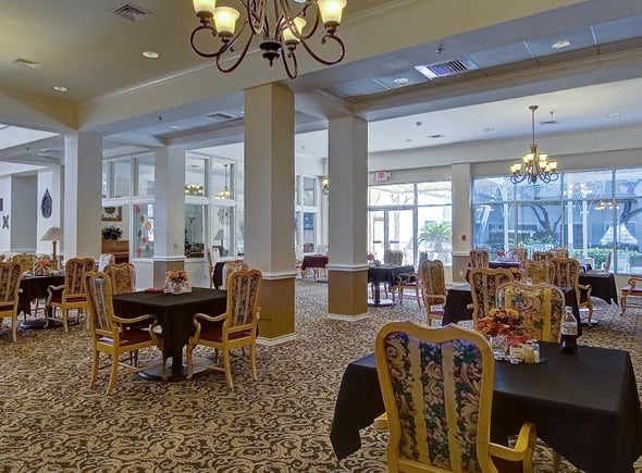 A lovely, elegant dining room with many tables and chairs, all set up with beautiful centerpieces and overlooking a sunny courtyard in Corpus Christi, Texas.