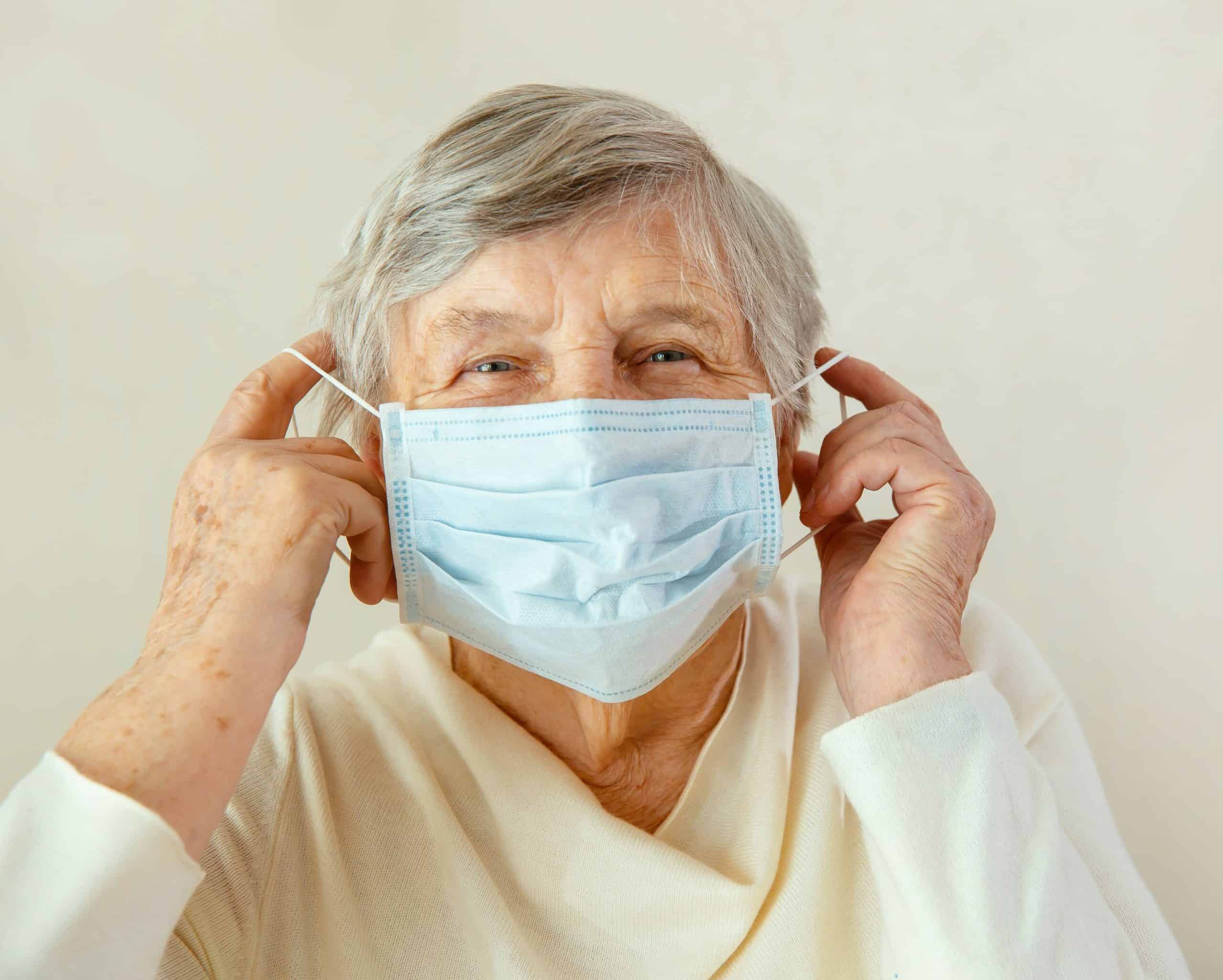 An elderly woman puts a medical mask on her face.