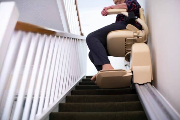 Senior Woman Sitting On Stair Lift At Home To Help Mobility