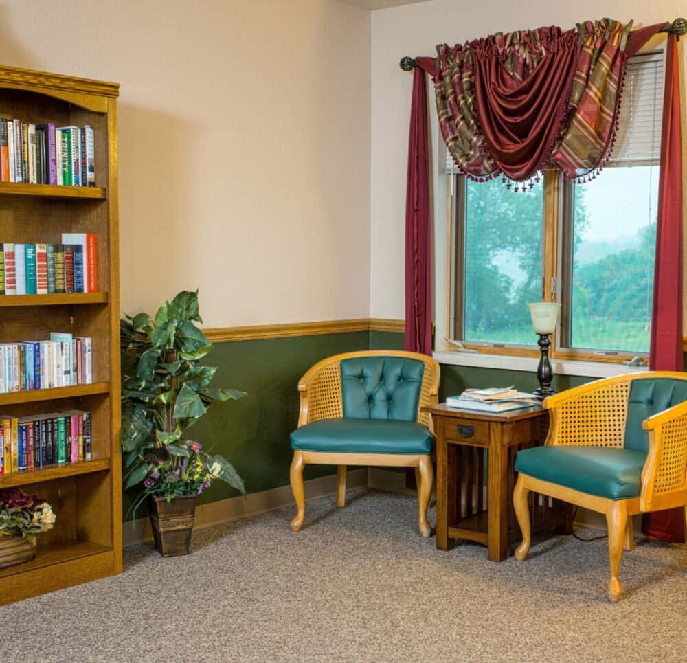 Library area with two chairs near a window at a senior living facility in Hartford, Wisconsin.