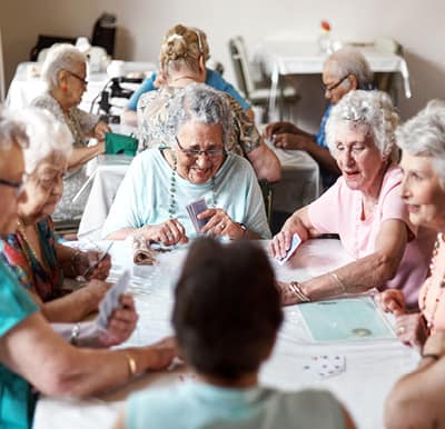 A group of senior women at a senior living community laughing over a game of cards in a well-lit activity room.