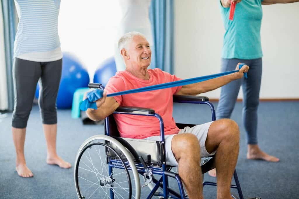 Senior in wheelchair exercising with exercising band during exercise class.