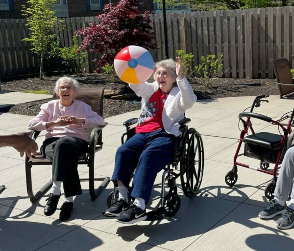Seniors in a memory care program sitting outside on patio playing a game.