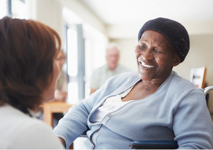 A senior living community resident smiling as her caregiver provides assistance.