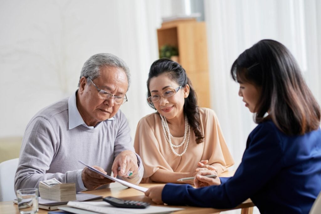 Loving senior couple sitting at spacious office and asking questions concerning an agreement