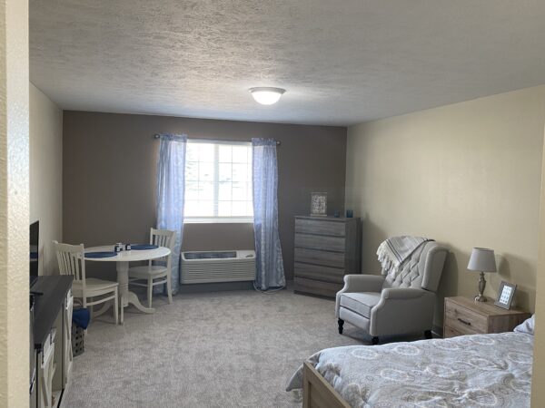 Apartment model with bed, chair, table and window at a senior living community in Plattsmouth, Nebraska.