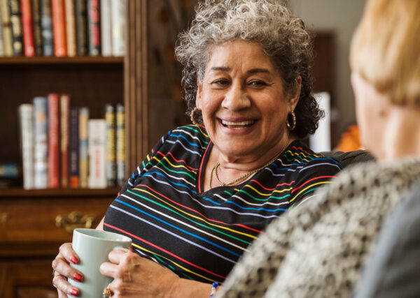 A senior woman and her friend enjoying a cup of coffee together in the library of a senior living community.