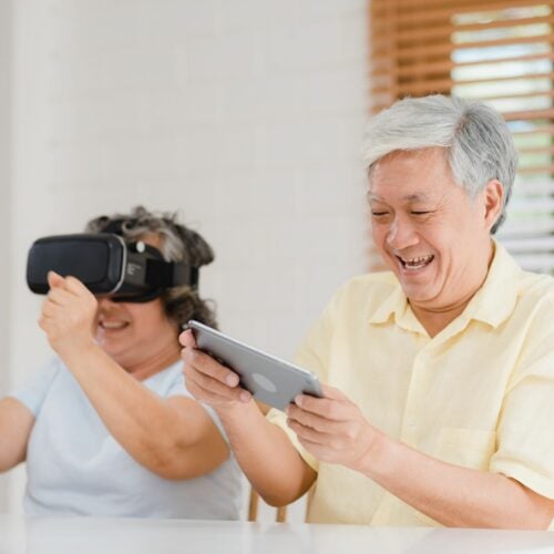 Asian elderly couple using tablet and virtual reality simulator playing games in living room, couple feeling happy using time together lying on table at home