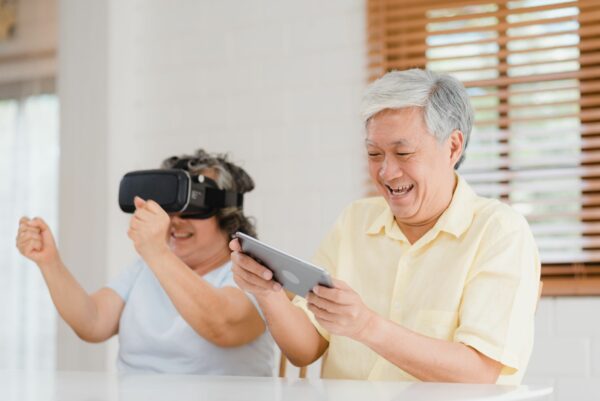 Asian elderly couple using tablet and virtual reality simulator playing games in living room, couple feeling happy using time together lying on table at home
