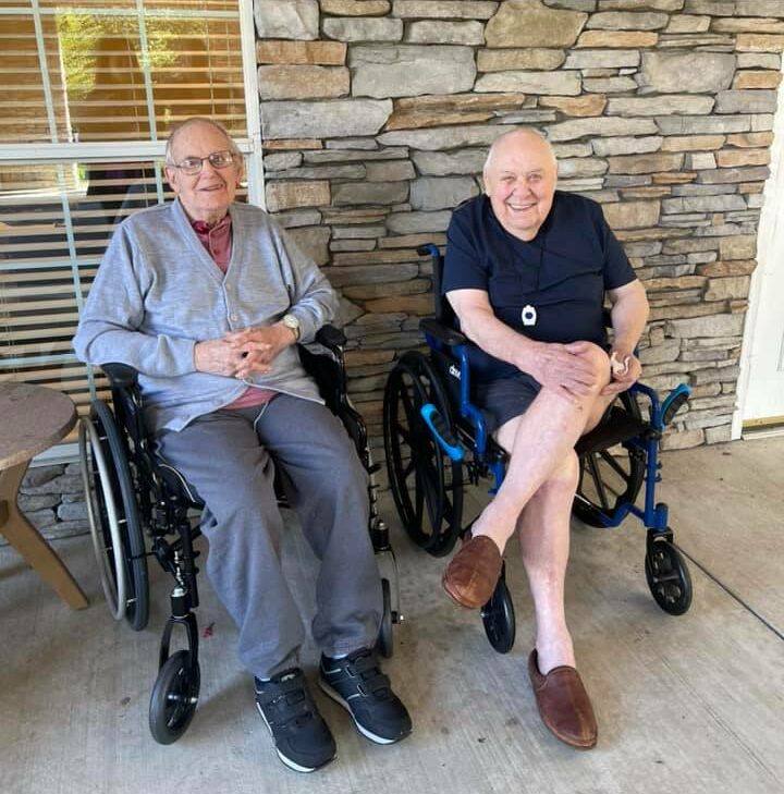 two senior men sit outside together and smile