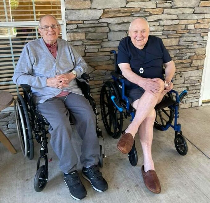 two senior men sit outside together and smile