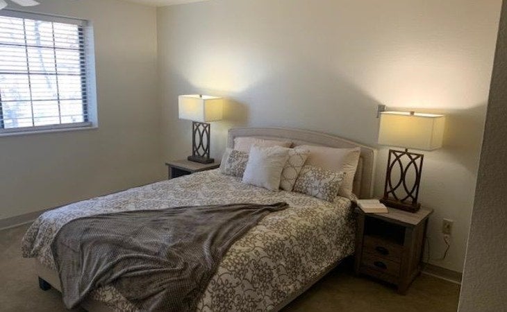 large bedroom area with two side tables, two lamps and bed near window