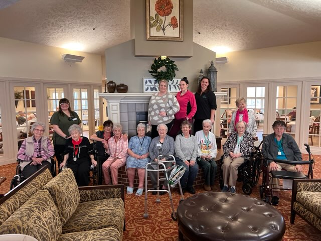 group of seniors and staff members smile at a gathering in the lobby