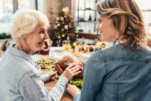 adult woman smiles while helping her senior mother