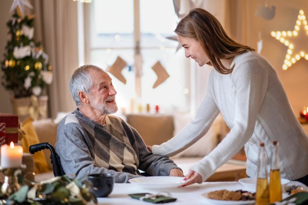 Young woman with senior grandfather in wheelchair indoors at home at Christmas
